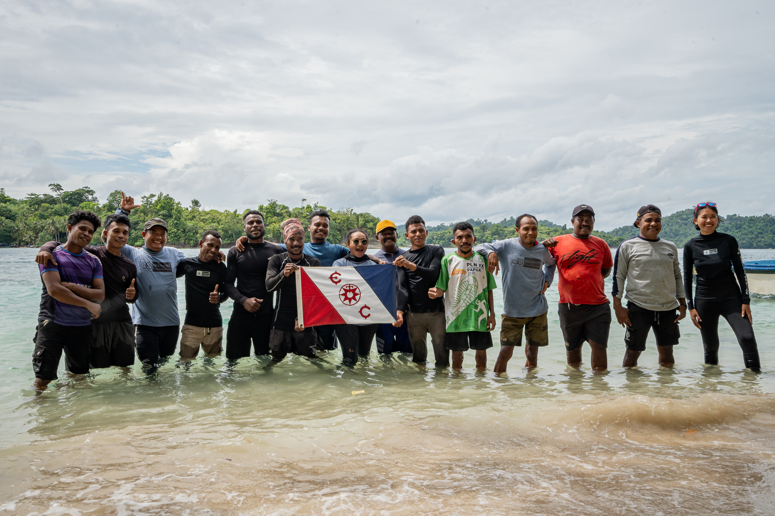 Expedition team in Misool, Indonesia, standing in shallow water holding dive flags and celebrating conservation partnership